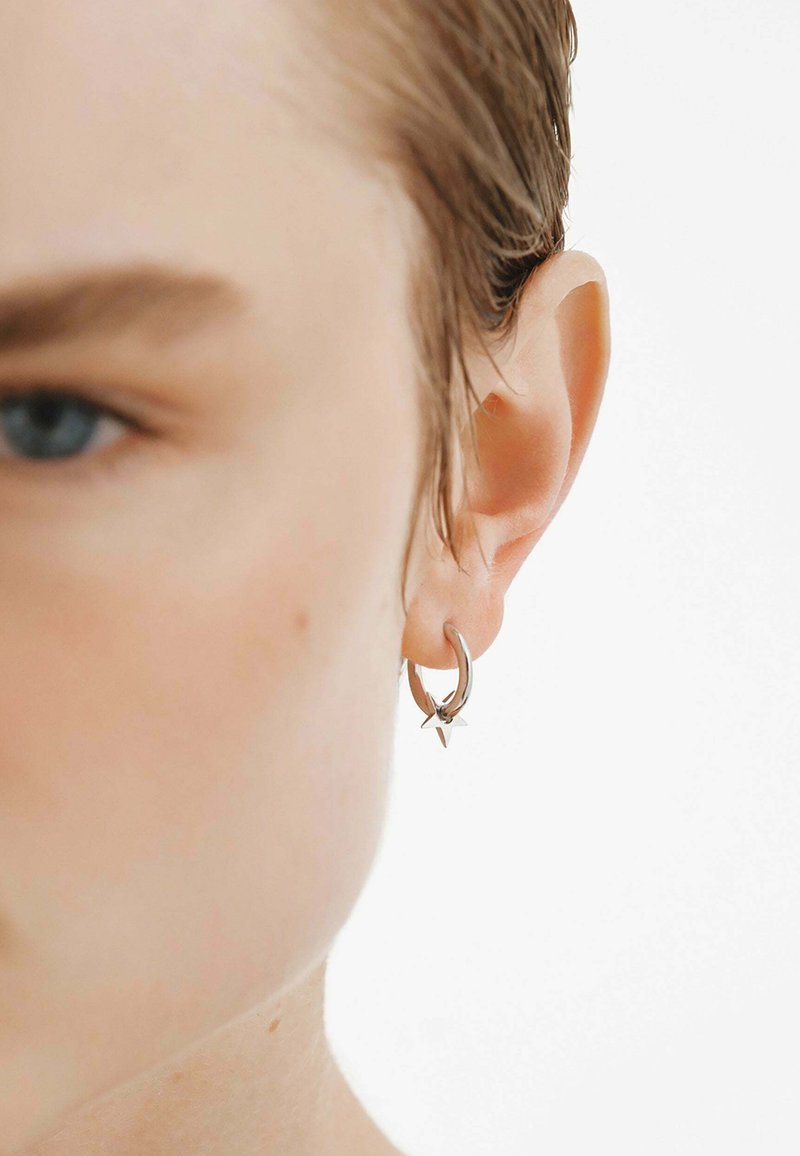 Pendientes de aro de plata con un pequeño colgante en forma de estrella, que destacan por su acabado pulido y un diseño simple y moderno.