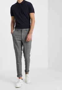 Polo shirt bleu marine associé à un pantalon à carreaux gris et des chaussures blanches. Le pantalon présente une coupe ajustée et des poignets retroussés.