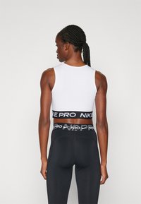 Bijela atletska crop majica s crnim Nike Pro pojasom. Crne uske tajice s Nike logom na pojasu. Glatka, rastezljiva tkanina.