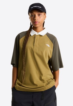 Polo verde oliva con cuello blanco, mangas cortas y logo de The North Face. Se lleva con pantalones oscuros, con bolsillos laterales y textura.