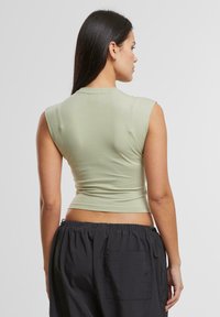 Lichtgroene cropped top met korte mouwen, aansluitend ontwerp, gemaakt van een gladde stof, gecombineerd met donkere, loszittende broek met een zak.
