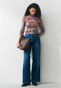 Top cu mânecă lungă, cu model, în nuanțe de mov și portocaliu, purtat cu blugi evazați, cu talie înaltă, de culoare albastră. Geantă de mână împletită, de culoare maro, și pantofi negri.