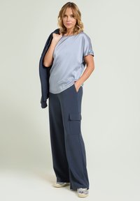 Lichtgrijze satin top met korte mouwen, gecombineerd met marineblauwe cargopants met wijde pijpen, zijzakken en een zachte textuur. Zilveren sneakers maken de look af.