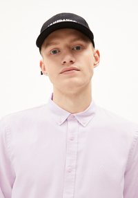 Lichtpaarse overhemden met lange mouwen, met een zachte textuur en een subtiele geborduurde logo op de borst. Zwarte pet met witte letters.