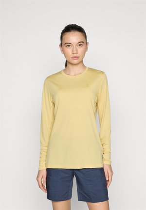 Long-sleeve, light yellow top made of soft, lightweight fabric; round neck; features a small logo on the chest; paired with navy shorts.