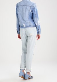 Giacca di jeans azzurro chiaro con dettagli strappati, abbinata a jeans azzurri chiari strappati. Scarpe col tacco blu con borchie decorative.