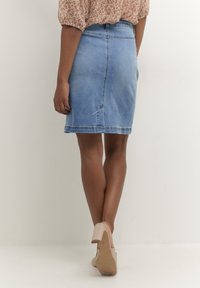 Světle modrá džínová sukně s upnutým pasem, zadním švem a rovný střihem. Kombinováno s světle zbarvenými botami na podpatku.