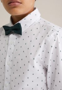 Bela srajca s kratkimi rokavi z drobnimi temnozelenimi vzorci dreves, v kombinaciji z usklajenim temnozelenim metuljcem. Gladek material in strukturiran ovratnik.