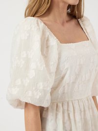Weißes Kleid mit floralem Stickmuster, Puffärmeln, quadratischem Ausschnitt und gerafftem Bund. Leichte, strukturierte Stoffqualität mit transparenter Optik.