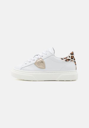 Zapatilla de cuero blanca con un emblema texturizado beige en el lado y un acento de estampado de leopardo en el talón. Suela de goma con una ligera plataforma.