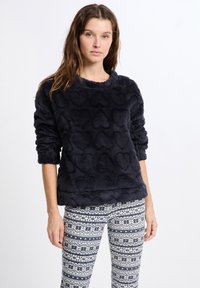 Marininblå fleece-pullover med upphöjda hjörn-mönster och långa ärmar, parat med vita och marinblå mönstrade leggings med snöflingor.