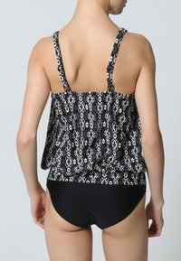 Schwarzes und weißes gemustertes Tankini-Oberteil mit verstellbaren Trägern, lockerer Passform und passendem schwarzen Bikiniunterteil. Glatte Stoffstruktur.
