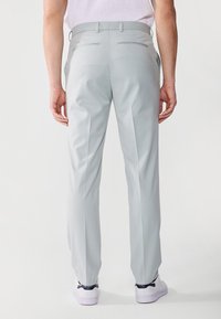 Pantaloni gri deschis cu un design croit, având buzunare la spate și o textură netedă. Purtați cu sneakers albi.
