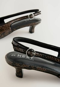 Talons slingback noirs et bruns avec un motif de serpent texturé, un talon bas et un détail en anneau métallique sur la bride.