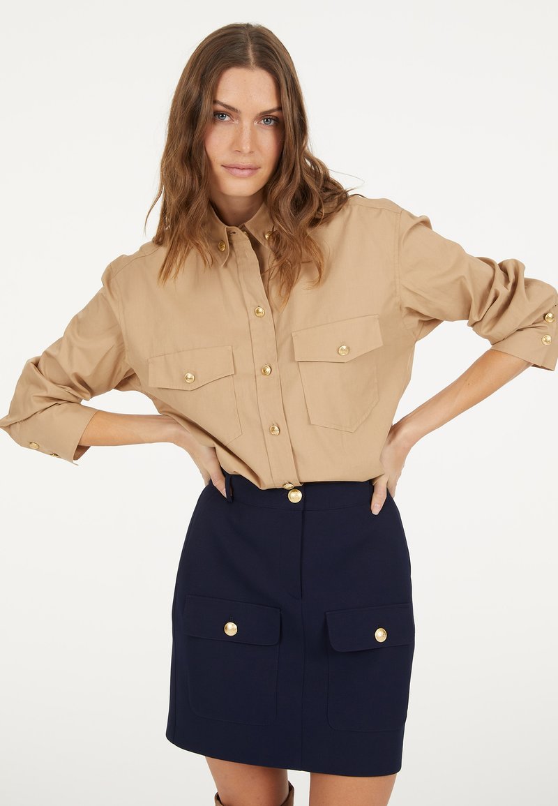 Beige button-up shirt with gold buttons and two chest pockets paired with a navy blue skirt featuring two front pockets and a gold button.