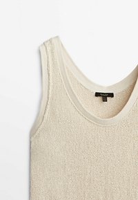 Débardeur sans manches de couleur crème en tricot avec des bords côtelés et un motif texturé, présenté à plat sur un fond blanc.