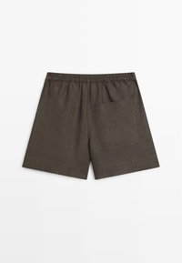 Brune løstsiddende shorts med elastisk taljebånd og en enkelt lomme på højre side, vist på en hvid baggrund.