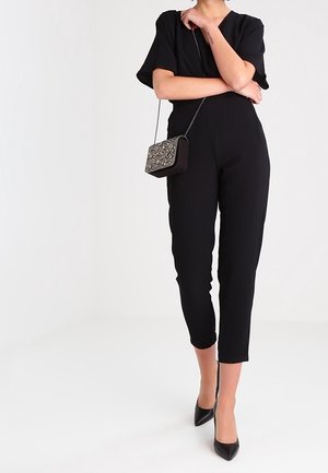 Svart jumpsuit med korta ärmar, slim fit, kort längd. Matchas med en mönstrad axelväska och svarta högklackade skor. Slät tygtextur.