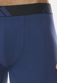 Blå träningsshorts med en slät yta och svart midjeband som har Adidas-logotypen och ett diagonalt randmönster.