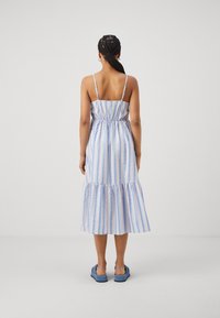 Randig midiklänning med tunna axelband, samlad midja och flerlagad nederdel, med blå och pastellfärger i ett mjukt tyg. Avslappnade skor synliga.