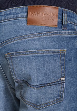 Blaue Jeans aus Denim mit einem rechteckigen braunen Lederpatch mit der Aufschrift "DAN JOHN" am hinteren Taillenbund und gelben Stickdetails an den Taschen.