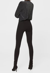 Svarta, figurnära leggings ihop med en kort, skimrande svart topp. Tyget har en subtil glans och en mjuk struktur. Svarta högklackade stövlar.