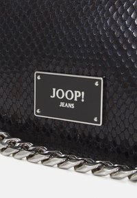 Sac à main en simili cuir de serpent noir, avec une bandoulière en chaîne argentée et une plaque en métal rectangulaire portant l'inscription "JOOP! JEANS" gravée.