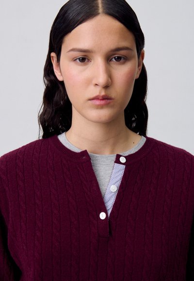 Pull en maille torsadée bordeaux avec un col henley, orné de détails rayés gris et bleu ainsi que de trois boutons blancs.