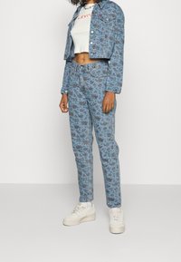 Blomsterprintet denimjakke og matchende jeans i lyseblå. Hvid cropped t-shirt med rød tekst. Hvide sneakers fuldender outfittet.