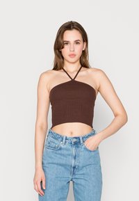 Top ligeiramente acastanhado, com textura canelada e design de pescoço halter. Apresenta um formato justo e abdómen exposto, combinado com jeans de cintura alta em azul claro.