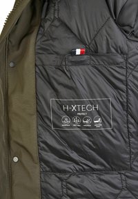 Olijfgroene parka met een zwarte gewatteerde voering. Bevat H-XTECH-label met details over waterbestendige, ademende en winddichte eigenschappen.