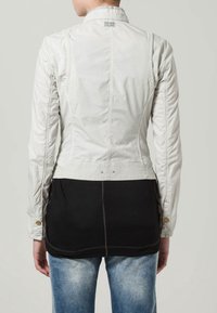 Jasnoszara kurtka o dopasowanym fasonie, z czarnym dolnym panelem i kontrastowymi przeszyciami, mankietami na guziki oraz wysokim kołnierzem.