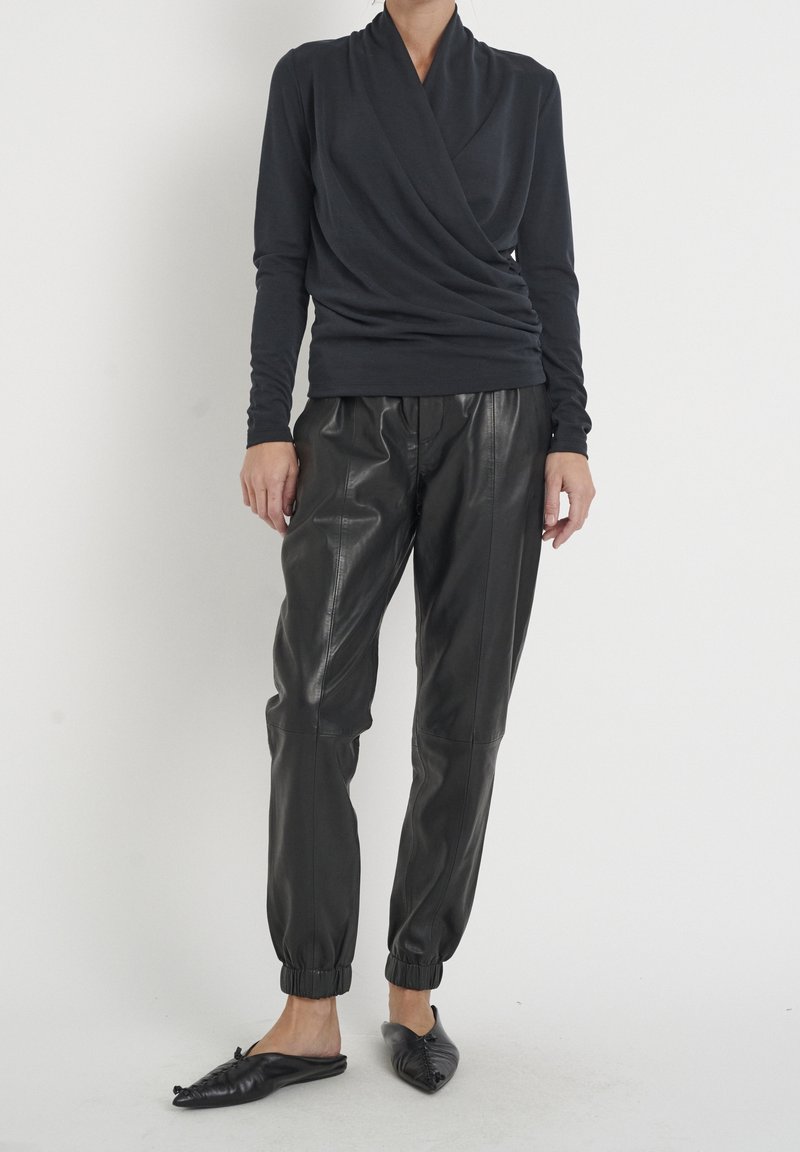 Haut à manches longues gris foncé avec un design drapé, associé à un pantalon en cuir noir style jogger avec des poignets froncés. Chaussures noires à enfiler.