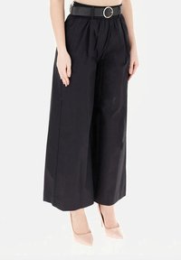 Pantaloni neri a gamba larga con vita arricciata, cinturati con una fibbia metallica rotonda. Texture liscia, vestibilità sartoriale e taglio alla caviglia.