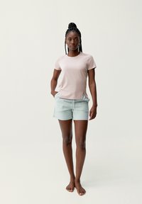 Svetlo ružová košeľa s krátkym rukávom a bočnými rozparokmi, skombinovaná so svetlozelenými šortkami s elastickým pásom a šnúrkou.