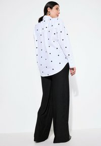 Witte overhemd met zwarte hartafdrukken, gecombineerd met wijde zwarte textured broeken. Heeft een klassieke kraag en lange mouwen.