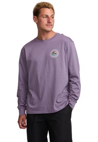 Long-sleeve, lavender shirt made from soft cotton. Features a round neck and a circular graphic patch with mountains in the center.