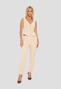 Beige vest with a deep V-neck and five golden buttons, paired with matching tailored pants and leopard-print high-heeled shoes.