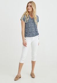 Top blu navy a maniche corte con un motivo ondulato, abbinato a pantaloni bianchi a vita alta con due bottoni laterali e mocassini beige.