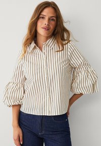 White button-up shirt featuring vertical brown stripes, a collared neck, and puffed sleeves. Paired with dark blue jeans.