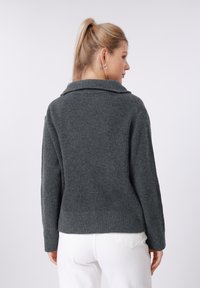 Γκρι πουλόβερ με ριμπ ύφανση, γιακά, μακριά μανίκια και άνετη εφαρμογή, φορεμένο πάνω από άσπρο τζιν. Ορατό υφασμάτινο πλεκτό υλικό με υφή.