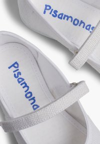 Zapatos de lona blancos con una correa texturizada y el logotipo azul de "Pisaamonas" en la plantilla. Diseño simple con suela plana, aptos para un uso casual.