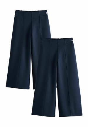 Zwei Paare marineblaue, weit geschnittene, verkürzte Hosen mit Nahtdetails und Knopfakzenten am Bund, auf weißem Hintergrund präsentiert.
