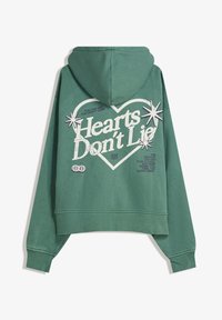 Zelena skrajšana kapuca iz mehkega blaga, ki ima grafiko srca s besedilom "Srca ne lažejo" in zvezdnate detajle na hrbtni strani.
