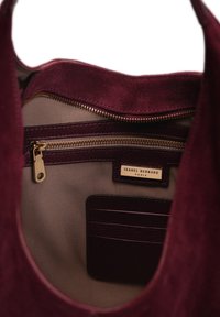 Maroon suede tote bag interior with beige lining, zip pocket, and leather card slots. Features metal zipper and gold brand tag.