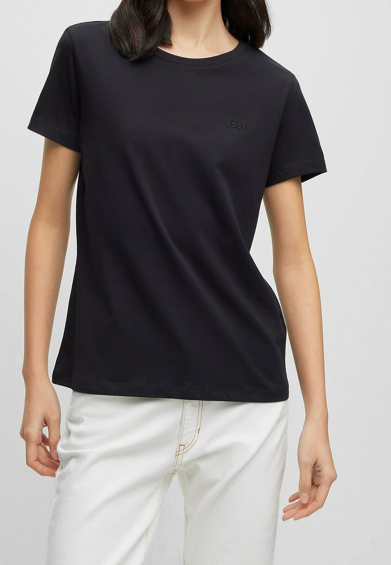 T-shirt nera in cotone con collo rotondo, maniche corte e logo "BOSS" tono su tono sul petto. Abbinata a pantaloni bianchi.