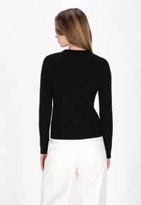 Zwarte gebreide trui met ribbeltextuur en lange mouwen, aansluitend ontwerp, van achteren weergegeven met lichtgekleurde broek.