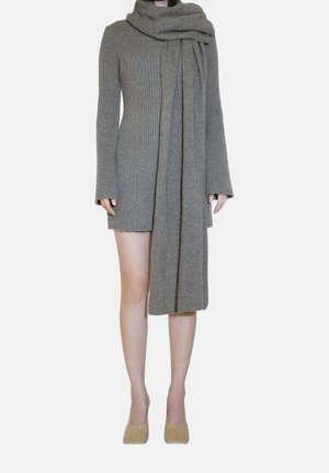 Femme portant une robe en maille côtelée grise à manches longues, une grande écharpe assortie et des chaussures à talons beiges, debout devant un fond blanc.