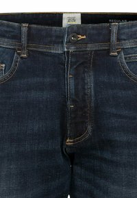 Mørkeblå denimjeans med kontrasterende gul syning, featuring en knaplukning og klassisk fem-lomme design.