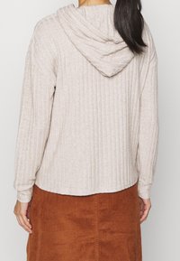 Sudadera beige con canalé y textura suave, con capucha, combinada con una falda de pana marrón. Costuras visible y mangas largas.